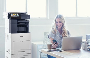Attractive woman working on a laptop computer. She is casually dressed  with long blonde hair. She looks relaxed with a cup of coffee and she is probably surfing the internet. She could be a business woman working at home or in an office. Shot is back lit with copy space. There is a digital tablet and she is texting on a smart phone.